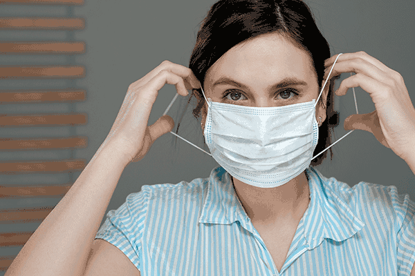 Young woman putting on a disposable surgical face mask